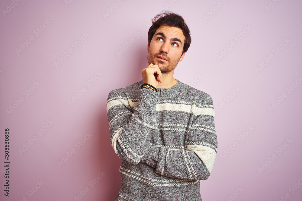 Young handsome man wearing casual striped sweater standing over isolated pink background with hand on chin thinking about question, pensive expression. Smiling with thoughtful face. Doubt concept. Young handsome man wearing casual striped sweater standing over isolated pink background with hand on chin thinking about question, pensive expression. Smiling with thoughtful face. Doubt concept.