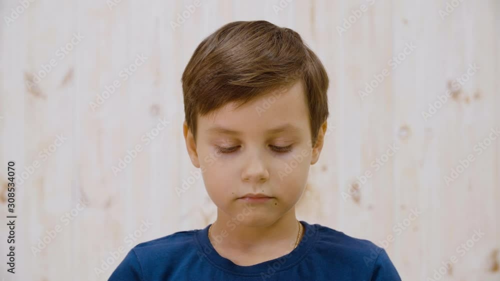 Portrait of adorable pensive boy looking down and winking. Close-up view of cute serious preteen boy standing and looking down indoors Portrait of adorable pensive boy looking down and winking. Close-up view of cute serious preteen boy standing and looking down indoors