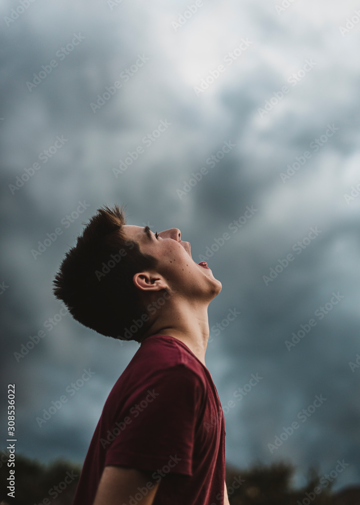 Teen boy looking up at dark cloudy sky with his mouth open wide. Teen boy looking up at dark cloudy sky with his mouth open wide.