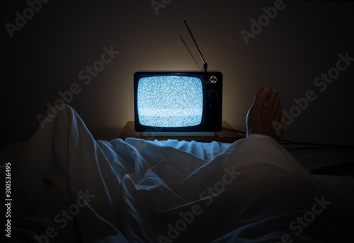 One person watches noise in TV in his bed with one foot sticking of the sheets photo
