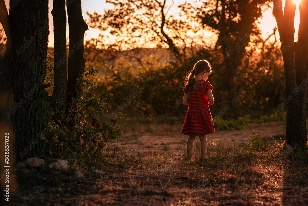Young girl pensive stands alone in golden light in between trees Young girl pensive stands alone in golden light in between trees