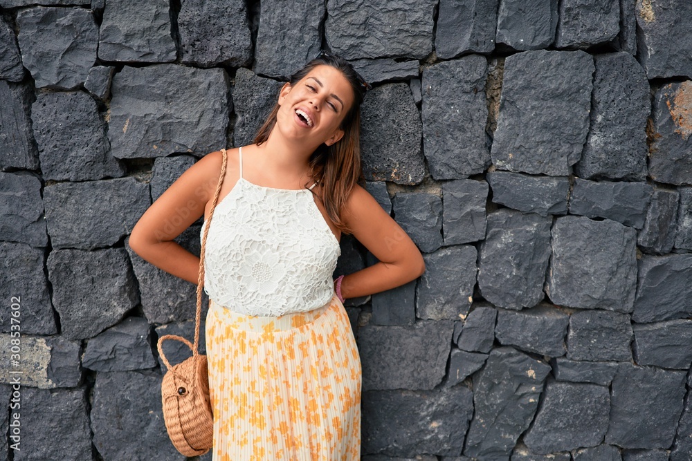 Beautiful girl leaning on the wall, young friendly woman smiling happy on a sunny day of summer Beautiful girl leaning on the wall, young friendly woman smiling happy on a sunny day of summer