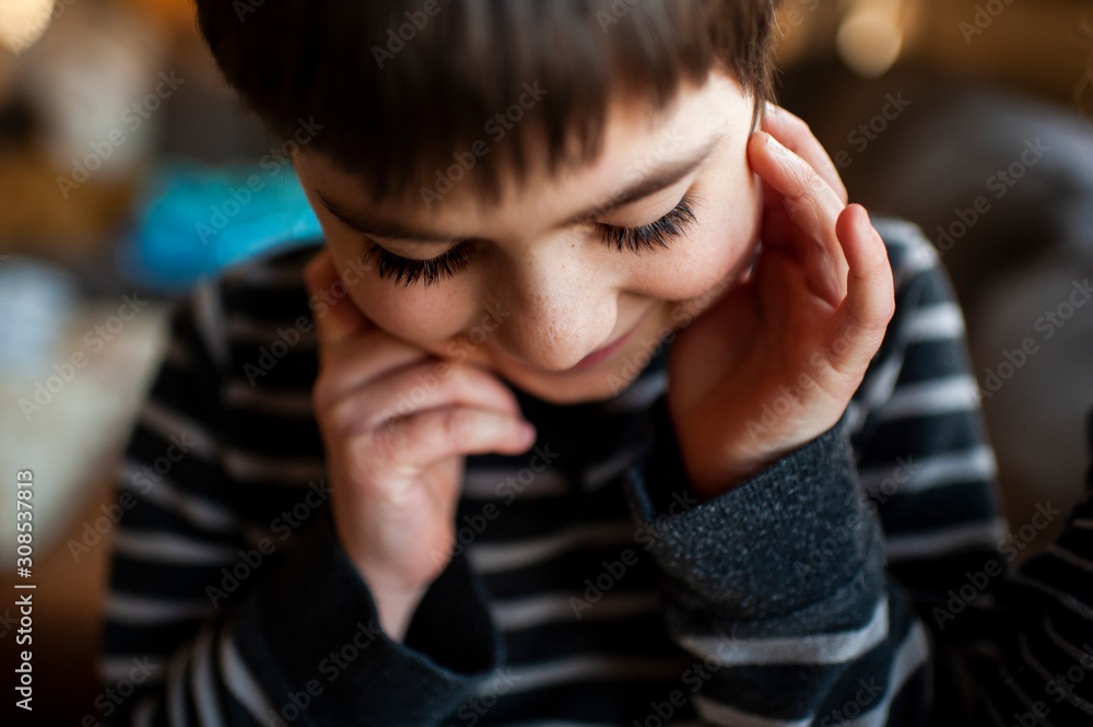 Boy 7-8 years old with long eyelashes looking down with hands by face Boy 7-8 years old with long eyelashes looking down with hands by face