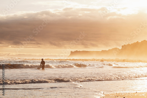 Tween boy holding a surfboard in the water during sunset photo