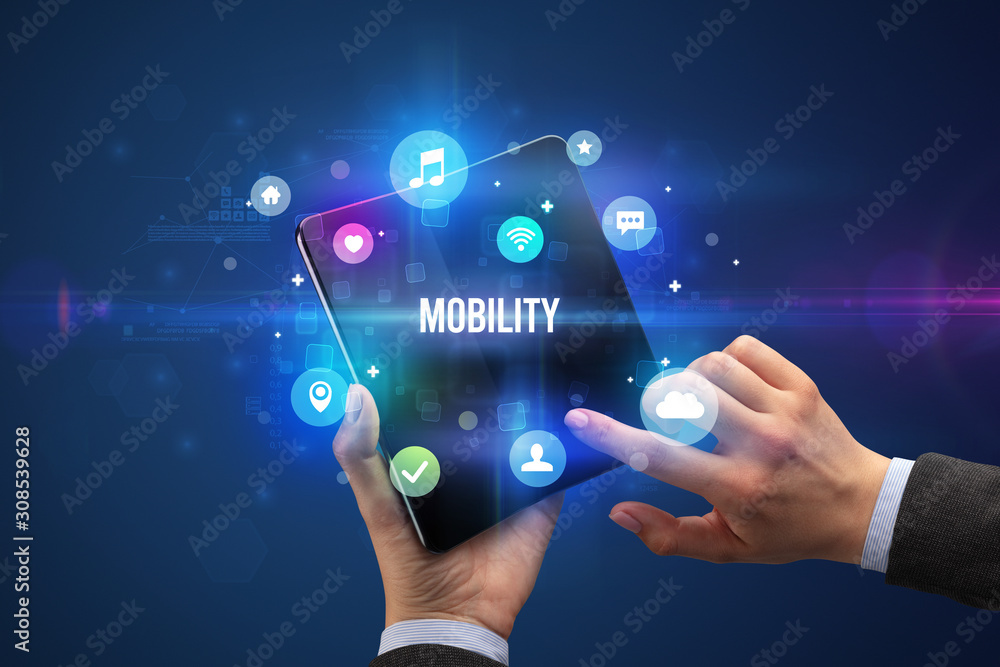 Businessman holding a foldable smartphone with MOBILITY inscription, social media concept Businessman holding a foldable smartphone with MOBILITY inscription, social media concept