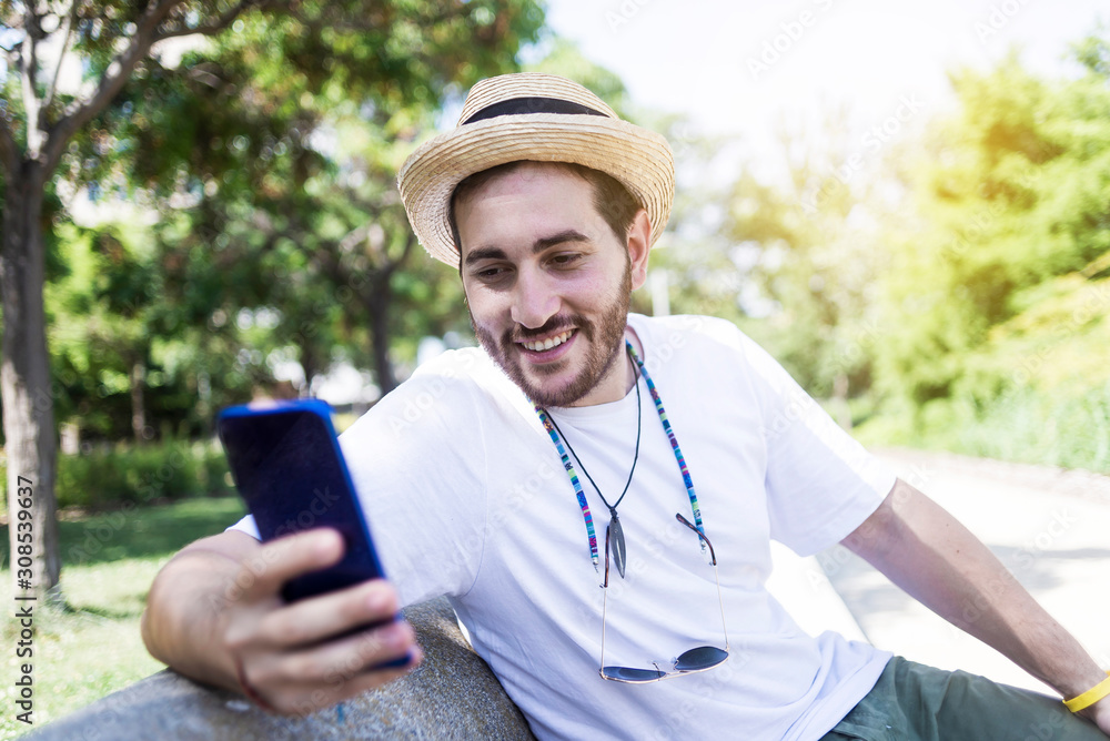 Smiling young bearded man sitting on bench using a smartphone Smiling young bearded man sitting on bench using a smartphone