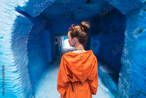 a female figure with her hair gathered in a bun, in a bright dress with a hood, stands with her back to the camera at the entrance to the tunnel in the blue city of Morocco © nelen.ru