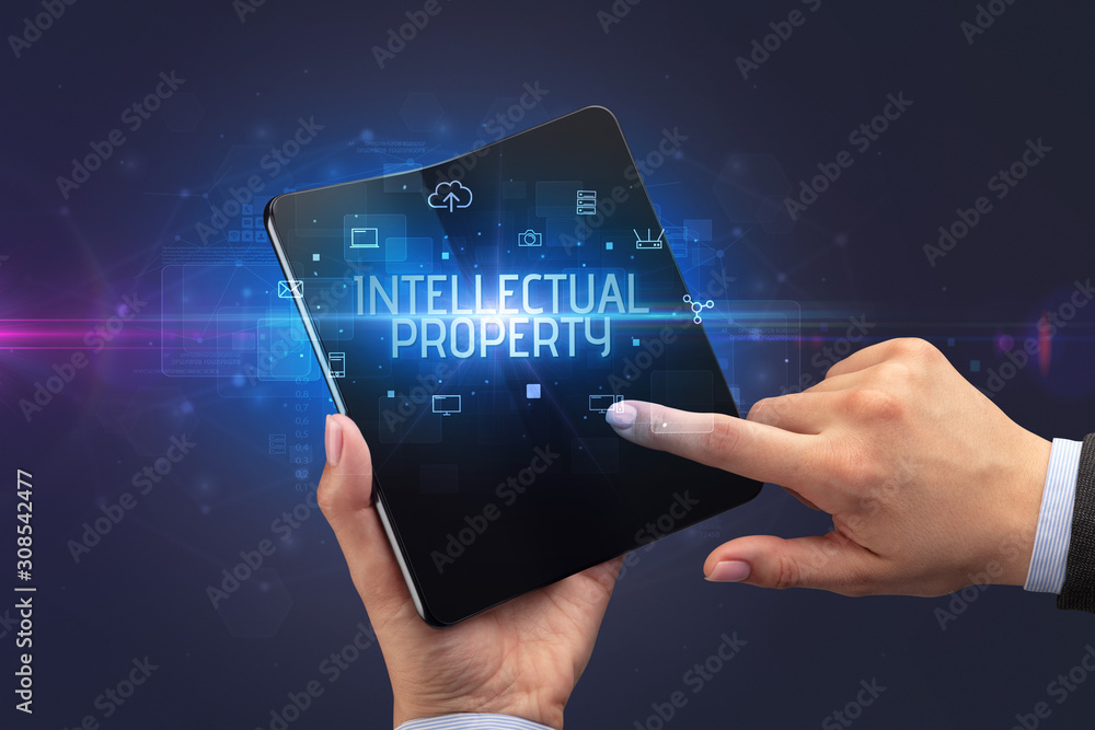 Businessman holding a foldable smartphone with INTELLECTUAL PROPERTY inscription, cyber security concept Businessman holding a foldable smartphone with INTELLECTUAL PROPERTY inscription, cyber security concept