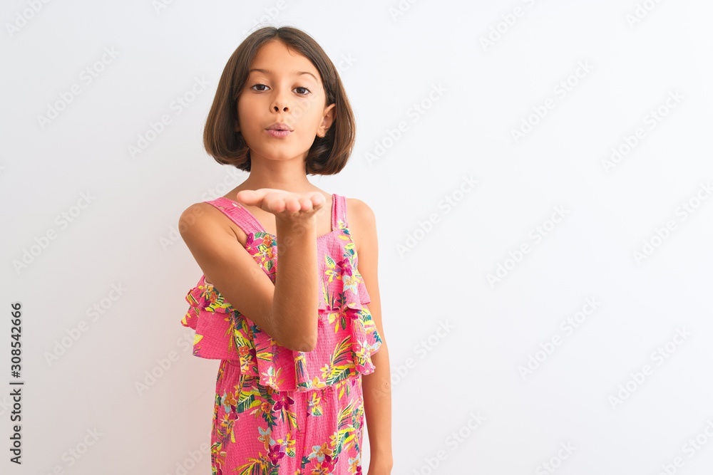 Young beautiful child girl wearing pink floral dress standing over isolated white background looking at the camera blowing a kiss with hand on air being lovely and sexy. Love expression. Young beautiful child girl wearing pink floral dress standing over isolated white background looking at the camera blowing a kiss with hand on air being lovely and sexy. Love expression.