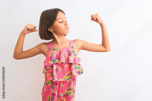 Young beautiful child girl wearing pink floral dress standing over isolated white background showing arms muscles smiling proud. Fitness concept.