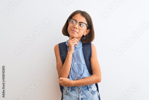 Beautiful student child girl wearing backpack and glasses over isolated white background with hand on chin thinking about question, pensive expression. Smiling with thoughtful face. Doubt concept.