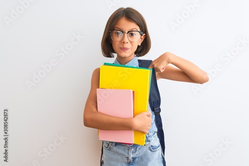 Beautiful student child girl wearing backpack glasses books over isolated white background with surprise face pointing finger to himself