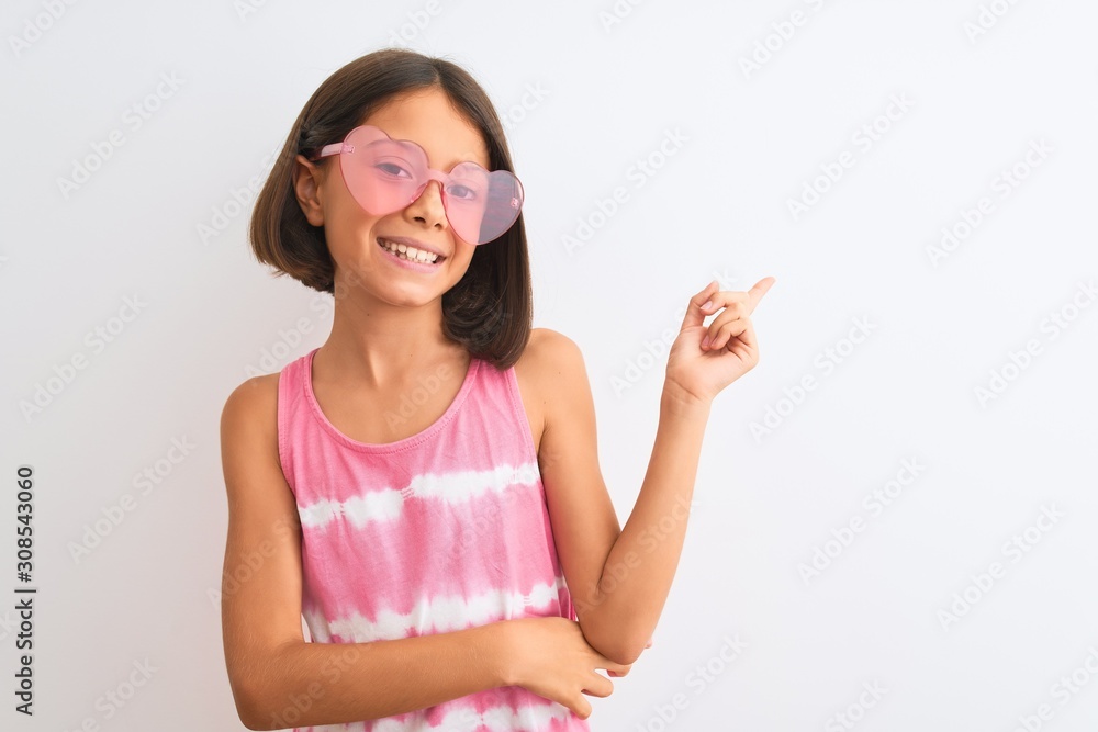 Young beautiful child girl wearing pink t-shirt and sunglasses over isolated white background with a big smile on face, pointing with hand and finger to the side looking at the camera. Young beautiful child girl wearing pink t-shirt and sunglasses over isolated white background with a big smile on face, pointing with hand and finger to the side looking at the camera.