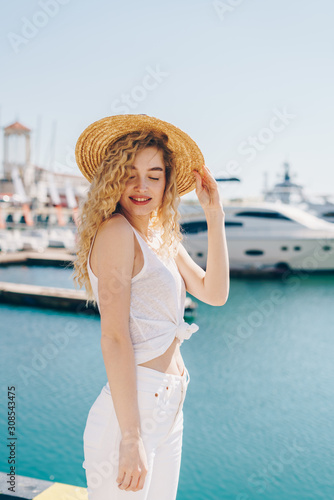 curly blonde smiles gently covering her eyes and holding her shoulders against the background of ships and the sea © nelen.ru