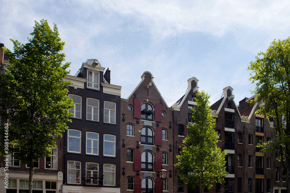 View of historical, traditional and typical buildings showing Dutch architectural style and trees in Amsterdam. It is a sunny summer day with blue sky.