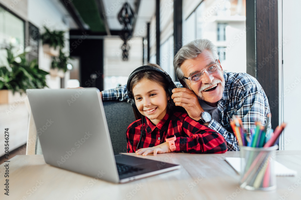 Funny old man with his granddaughter using laptop for play game with headphones. Funny old man with his granddaughter using laptop for play game with headphones.