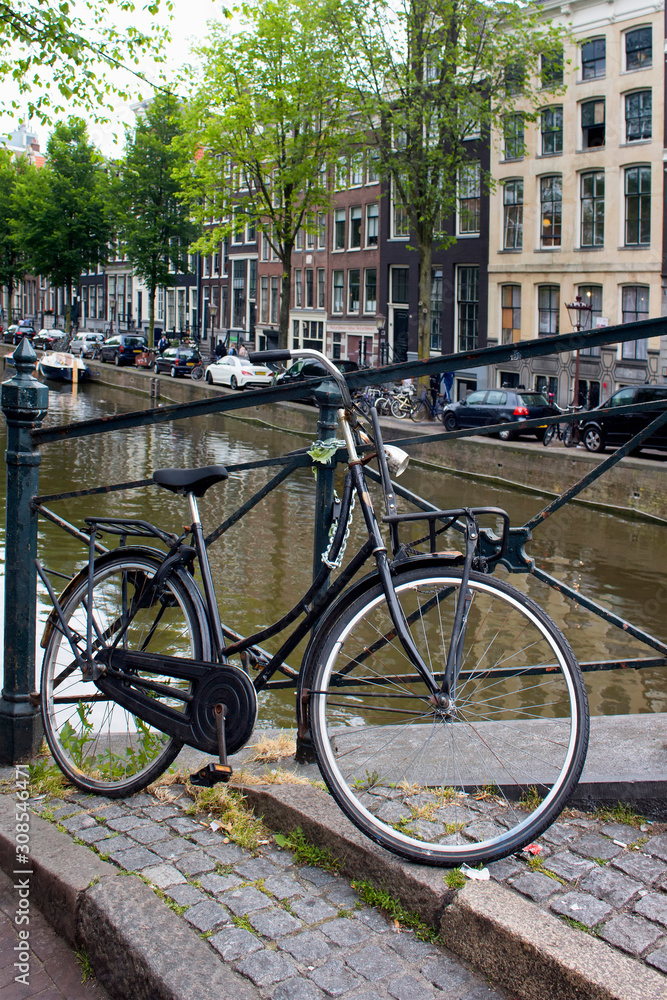 Close up view of parked bicycle in Amsterdam. Canal, trees, cars and historical and traditional buildings are in the background. It is a summer day