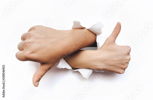 Like and dislike. Thumbs up and down sign of a man's and woman hand. The wrist came out through the torn hole in white paper and shows fingers up and down. Bad and good concept.