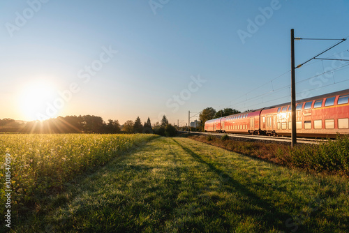 Passenger train and rapeseed field. Spring landscape at sunrise