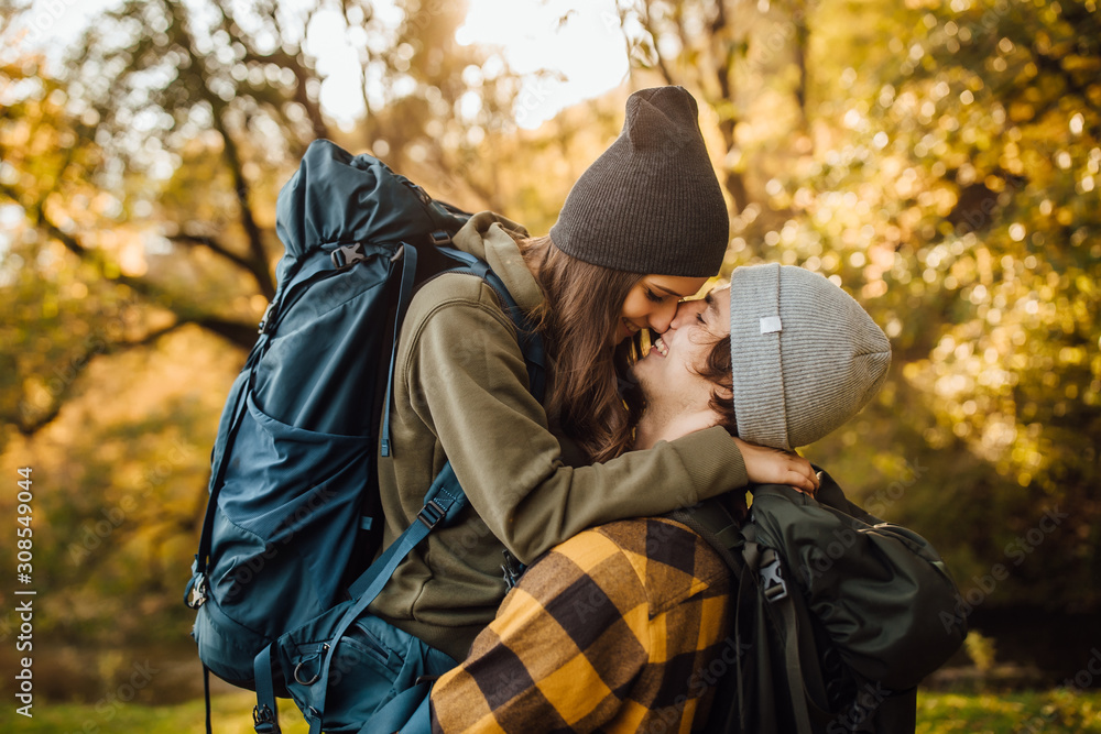 Young beautiful couple with hiking backpack kissing in the forest. Attractive woman and handsome man relaxing together in nature. Young beautiful couple with hiking backpack kissing in the forest. Attractive woman and handsome man relaxing together in nature.