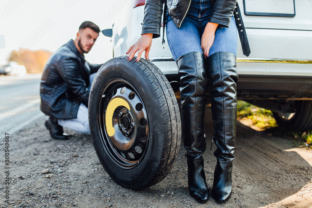 Fototapeta premium Man mechanic changing tire that are leaking his car broke down at woman car, cropped image.