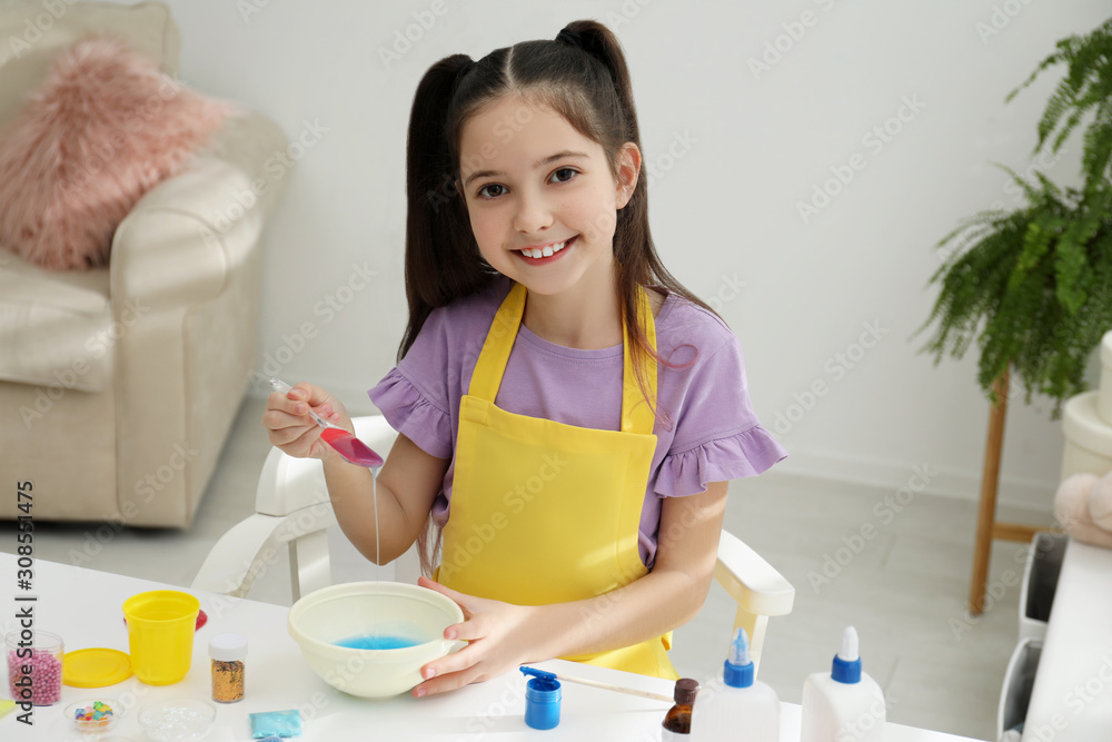 Cute little girl mixing ingredients with silicone spatula at table in room. DIY slime toy Cute little girl mixing ingredients with silicone spatula at table in room. DIY slime toy