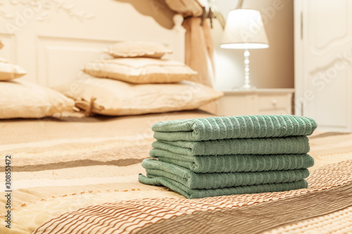 Stack of green hotel towel on bed in bedroom interior