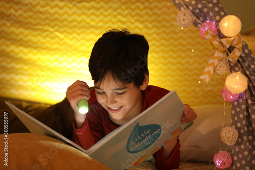 Boy with flashlight reading book in play tent at home