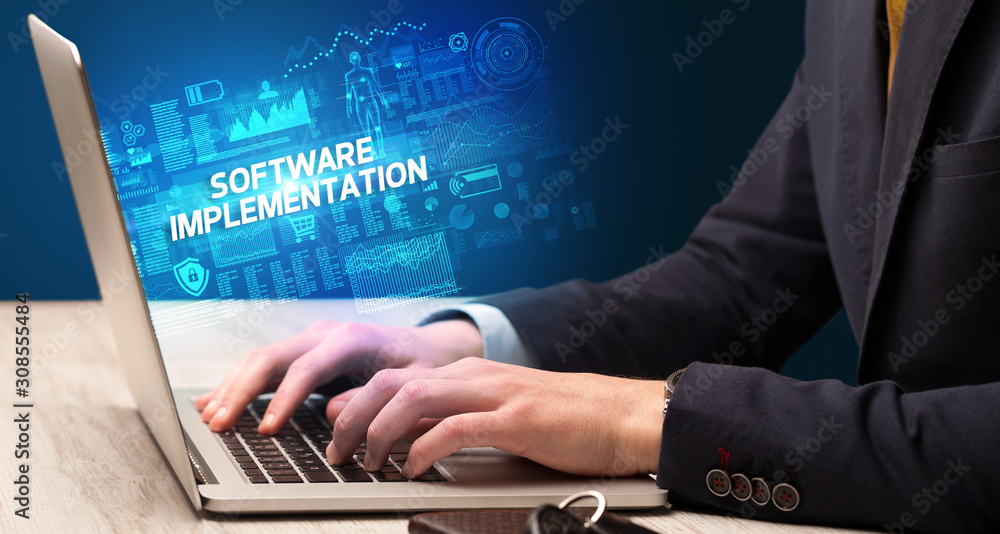 Businessman working on laptop with SOFTWARE IMPLEMENTATION inscription, cyber technology concept Businessman working on laptop with SOFTWARE IMPLEMENTATION inscription, cyber technology concept