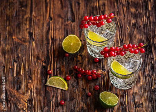 Fototapeta Naklejka Na Ścianę i Meble -  Gin Tonic with red currants, ice and lime, on a wooden background. View from above.