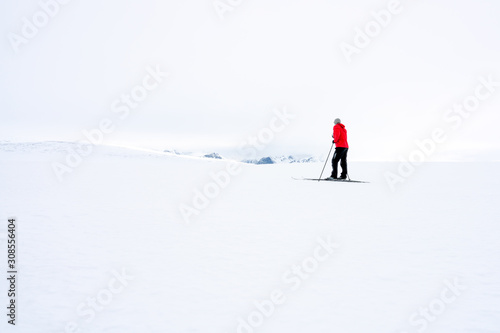 Man in red jacket doing cross country skiing during foggy weather in the mountains of Norway, looking towards the beautiful mountain scenery landscape. Freedom, sports, active and outdoors concept.
