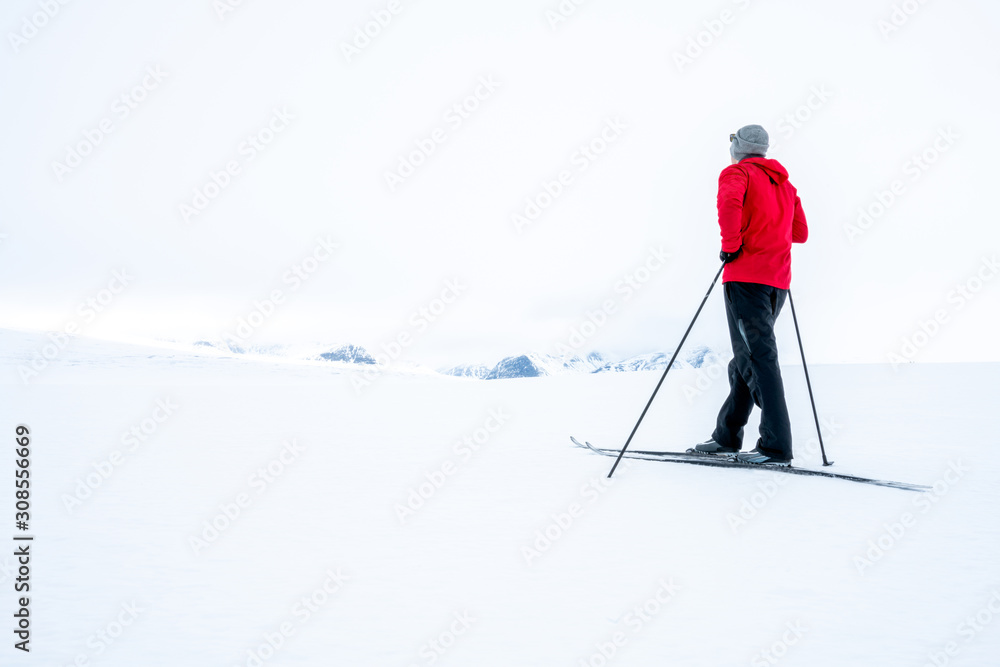Man in red jacket doing cross country skiing during foggy weather in the mountains of Norway, looking towards the beautiful mountain scenery landscape. Freedom, sports, active and outdoors concept. Man in red jacket doing cross country skiing during foggy weather in the mountains of Norway, looking towards the beautiful mountain scenery landscape. Freedom, sports, active and outdoors concept.