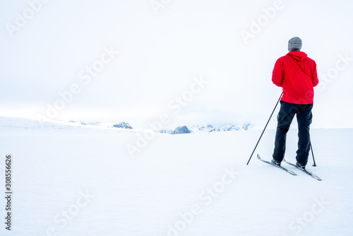 Man in red jacket doing cross country skiing during foggy weather in the mountains of Norway, looking towards the beautiful mountain scenery landscape. Freedom, sports, active and outdoors concept.