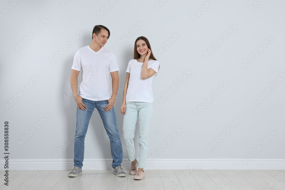 Young couple in stylish jeans near light wall Young couple in stylish jeans near light wall