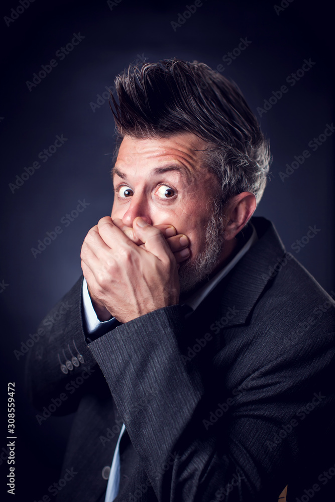 A portrait of shocked bearded man with iroquois wearing suit closed mouth with hands. People and emotions concept A portrait of shocked bearded man with iroquois wearing suit closed mouth with hands. People and emotions concept