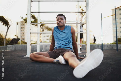 Portrait of a tired fitness african american young man sitting on outdoor public park ground taking rest after workout training