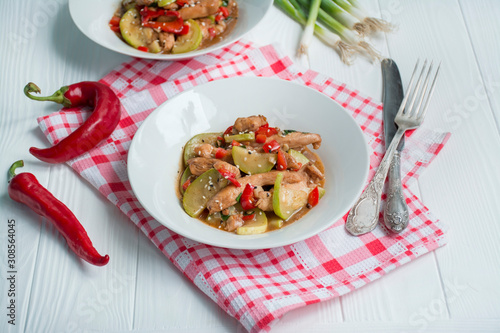 Hot salad with chicken, zucchini and chili pepper, sprinkled with sesame seeds and herbs. Asian food. Light wooden background.