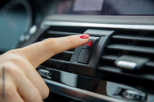 a female hand press the alarm light button on the dashboard of a car. close-up, soft focus, in the background car interior details in blur, side view