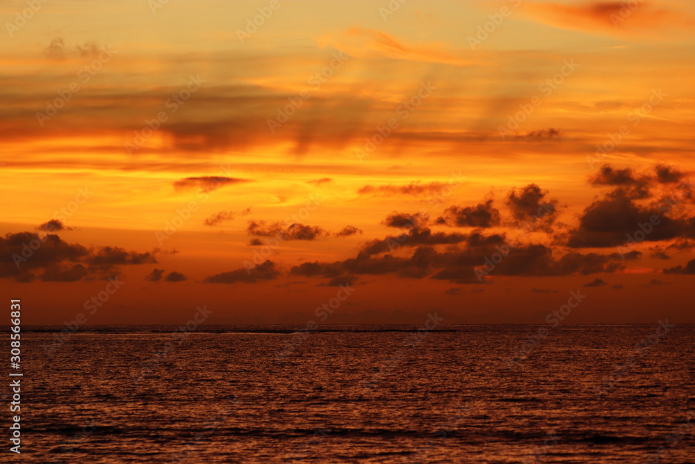 Sunset on a beach, evening sea background. Dark water and dramatic orange sky with clouds on the horizon, concept of romantic travel