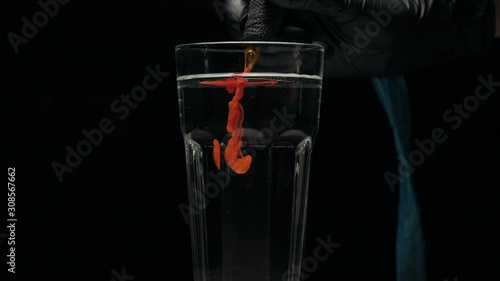 Close-up of tattoo machine cleaning slow is washed with needles in clear water from pigment of red paint.