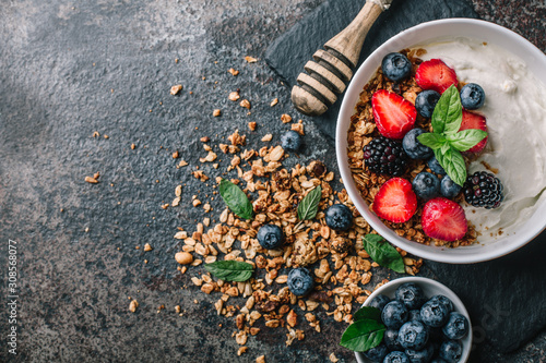 Healthy breakfast with granola, yogurt, fruits, berries on dark metal background. Summer homemade breakfast.