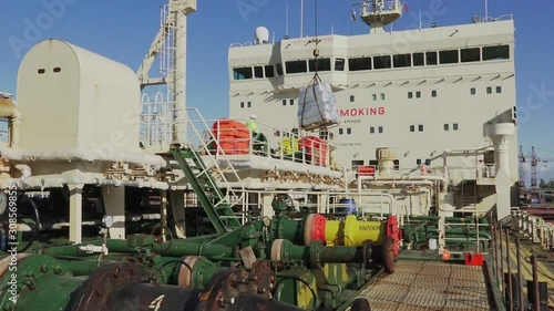 loading pallet with foodstuff onto oil tanker deck with powerful crane before leaving harbor under clear sky on autumn day photo