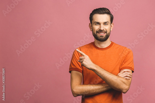 Look over there! Happy young handsome man in casual pointing away and smiling while standing against pink background.