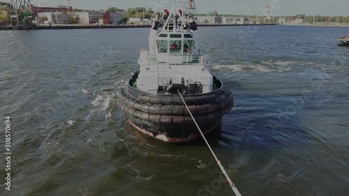 modern tugboat draws with rope oil tanker leaving tranquil harbor port from mooring berth near large city on sunny day