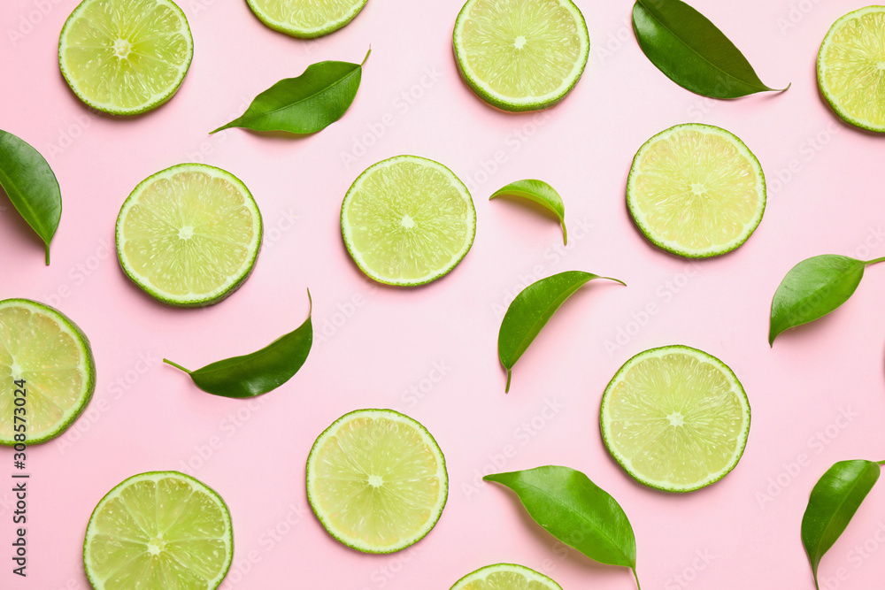 Juicy fresh lime slices and green leaves on pink background, flat lay