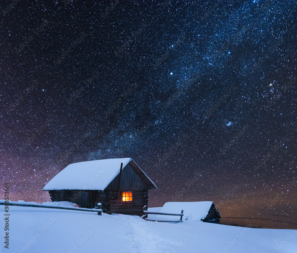 Dramatic wintry scene with snowy house with warm light in window. Fantastic night landscape glowing by milky way. Winter in Carpathian mountains, Ukraine, Europe Dramatic wintry scene with snowy house with warm light in window. Fantastic night landscape glowing by milky way. Winter in Carpathian mountains, Ukraine, Europe