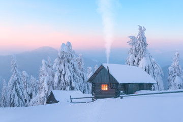 Fantastic winter landscape with wooden house in snowy mountains. Smoke comes from the chimney of snow covered hut. Christmas holiday and winter vacations concept