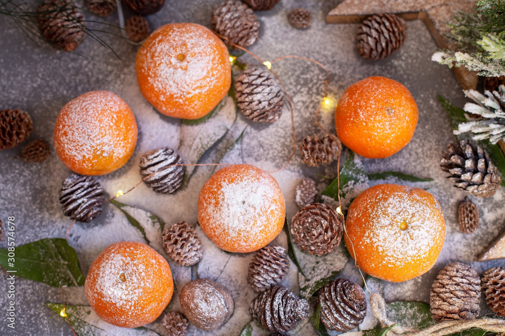 Orange tangerines on grey background in New Year's decor with brown pine cones and green leaves. Christmas decoration with mandarins. Delicious sweet clementine. Orange tangerines on grey background in New Year's decor with brown pine cones and green leaves. Christmas decoration with mandarins. Delicious sweet clementine.