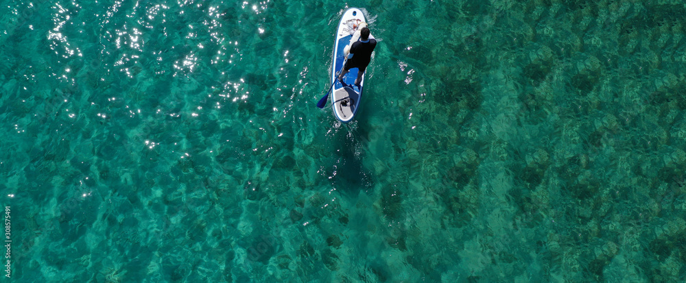 Aerial drone ultra wide panoramic photo of unidentified fit man paddling with his cute dog on a SUP board or Stand Up Paddle board in tropical exotic emerald bay