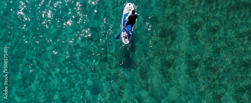 Aerial drone ultra wide panoramic photo of unidentified fit man paddling with his cute dog on a SUP board or Stand Up Paddle board in tropical exotic emerald bay